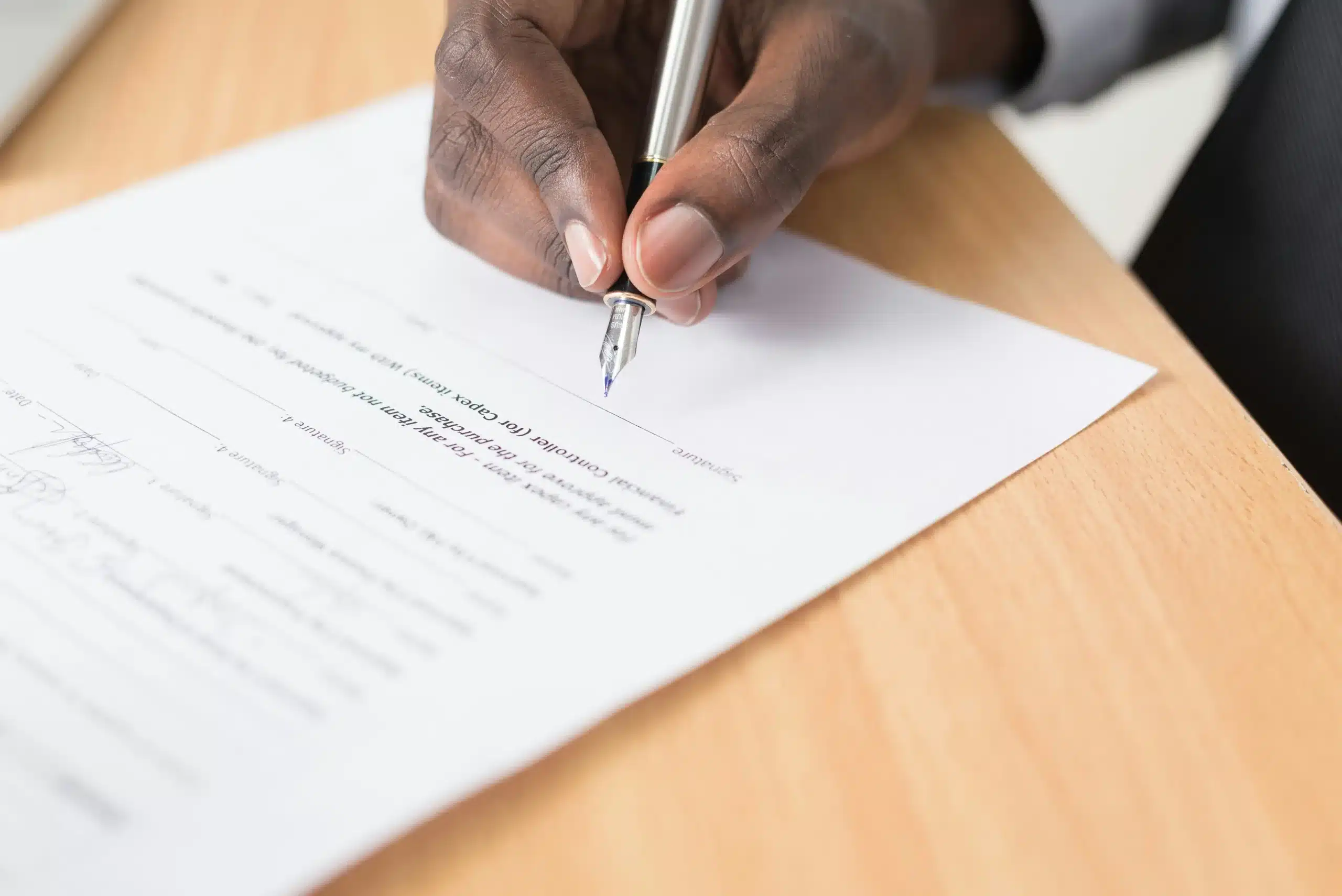 Mano firmando un contrato sobre un escritorio de madera